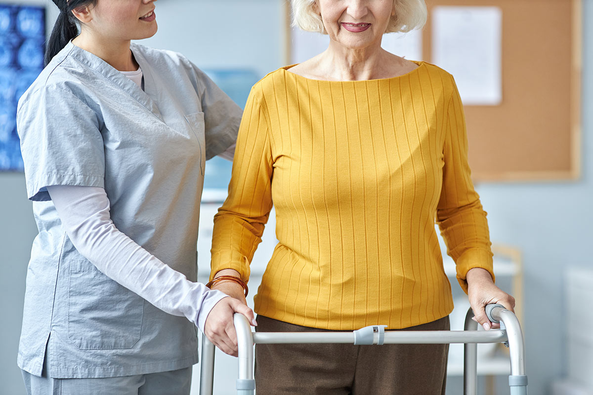 An in home caregiver helping a senior woman walking with a walker